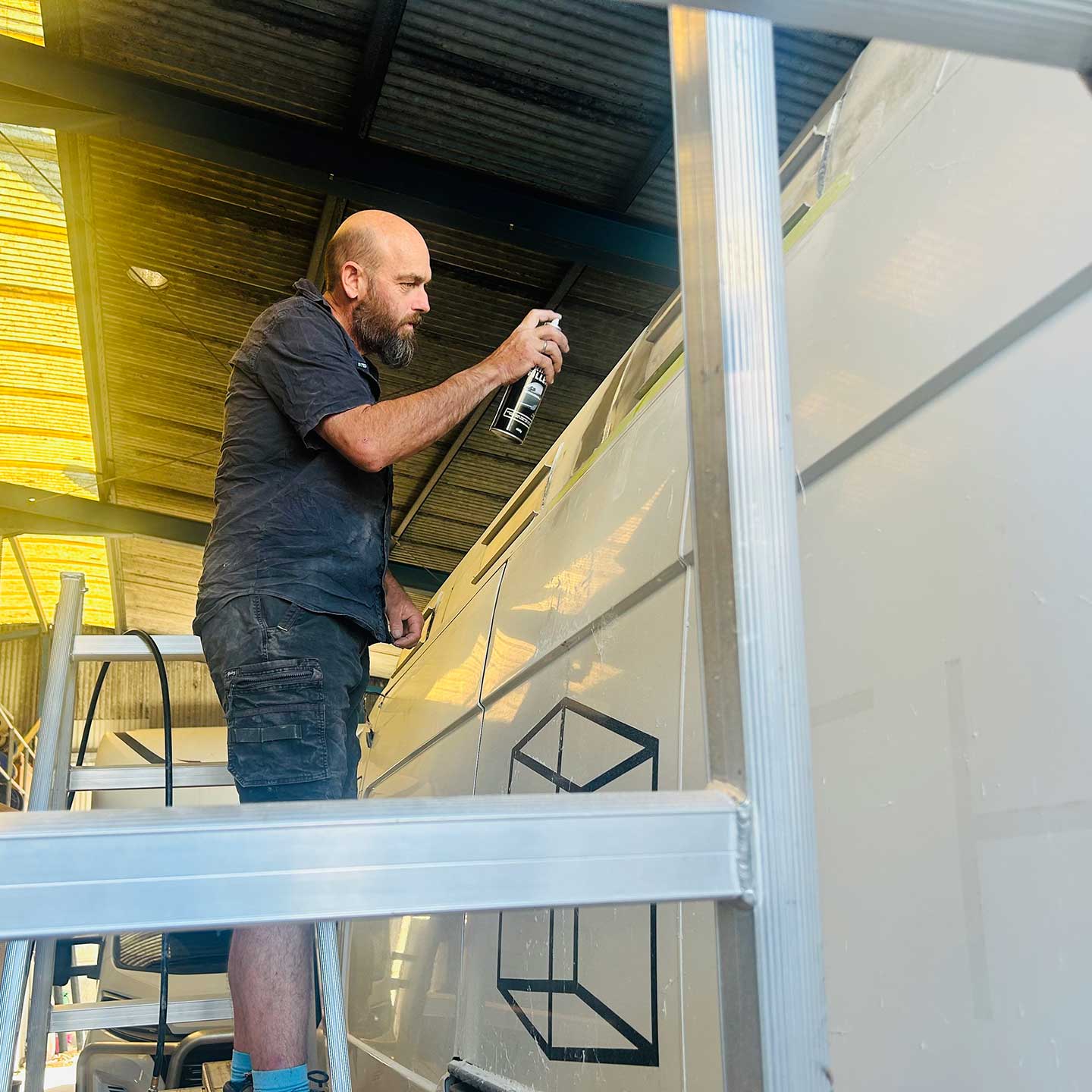 A man standing on a ladder spray painting the side of a van
